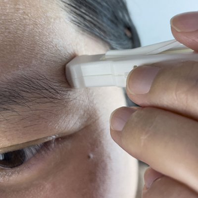 A small white plastic device being held to a man's forehead